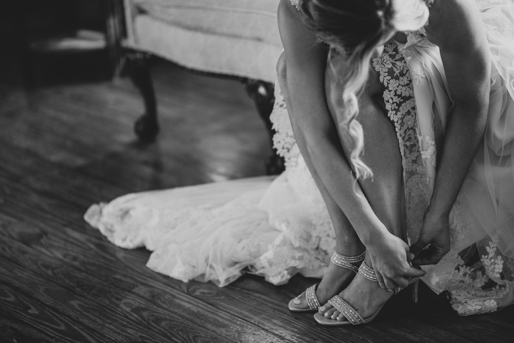 Black and white photo of a bride bending to buckle up her shoe