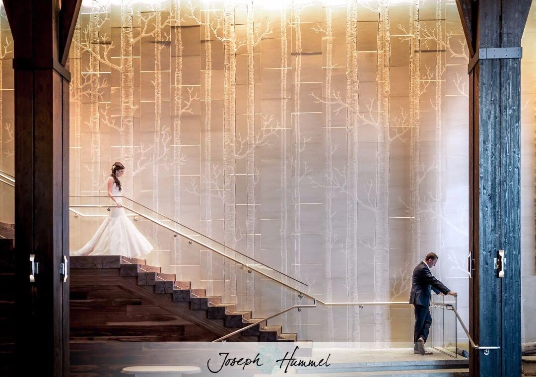 The first look moment of a bride walking down the stairs as the groom waits looking at the other side