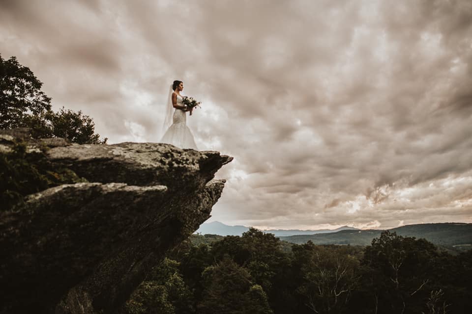 A bride holding a bridal bouquet posing on top of a cliff