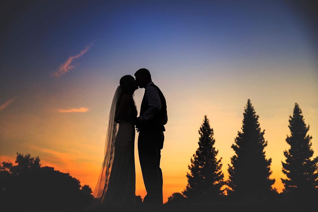 Silhouette of a bride and groom kissing with trees in the background