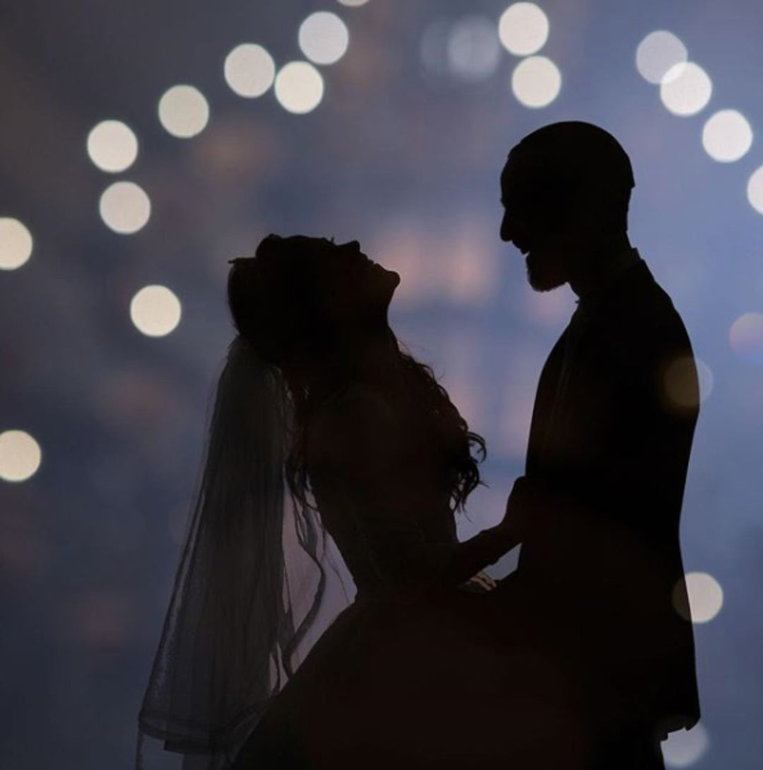 Silhouette of the bride and groom as they hold each other with a bokeh background