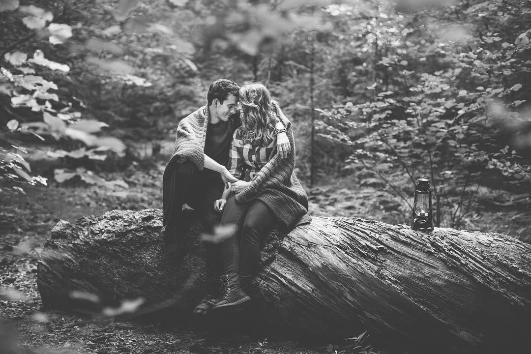 black and white image of a man and woman sitting on a rock cuddling