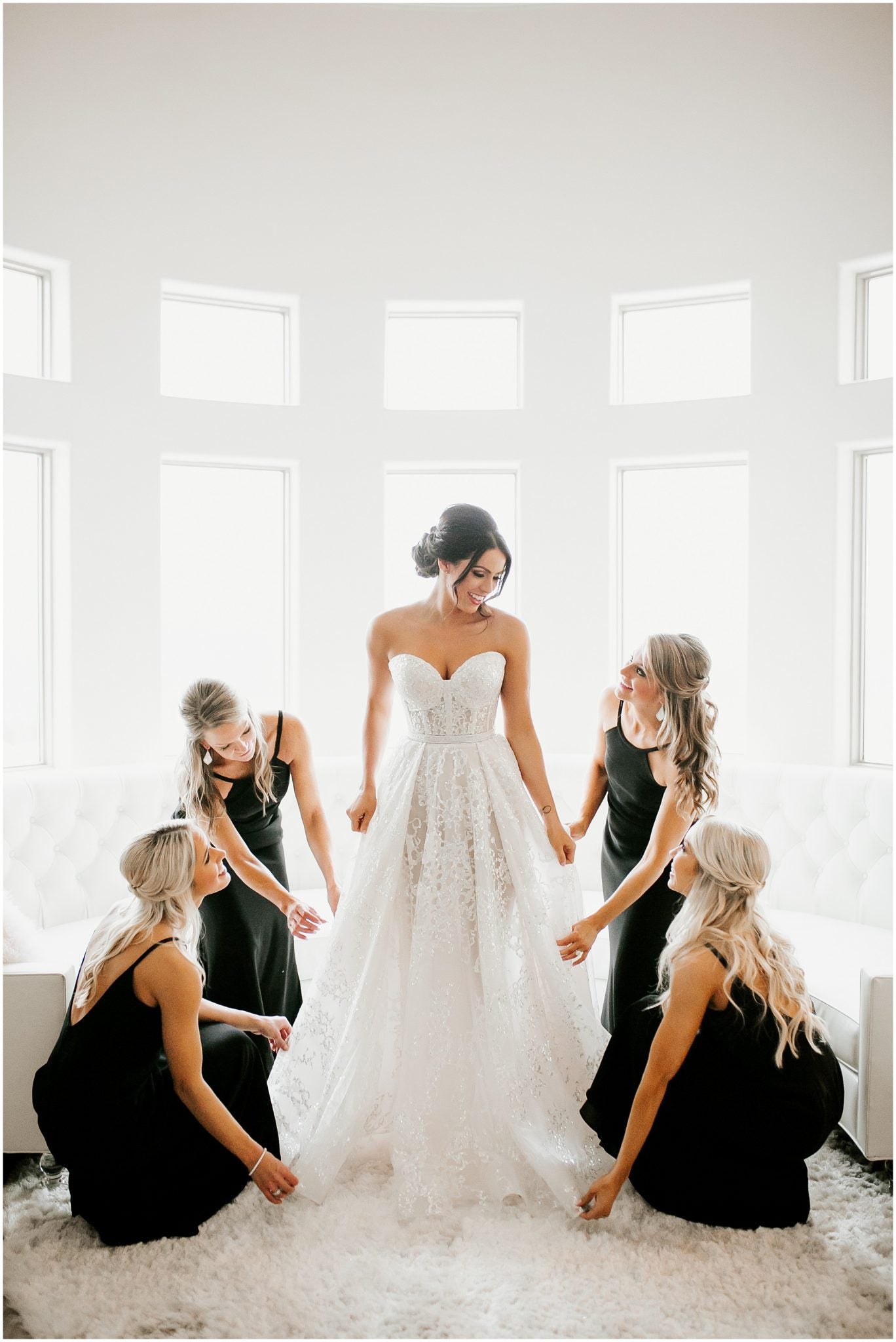 A bride posing in the center with bridesmaids holding her wedding dress