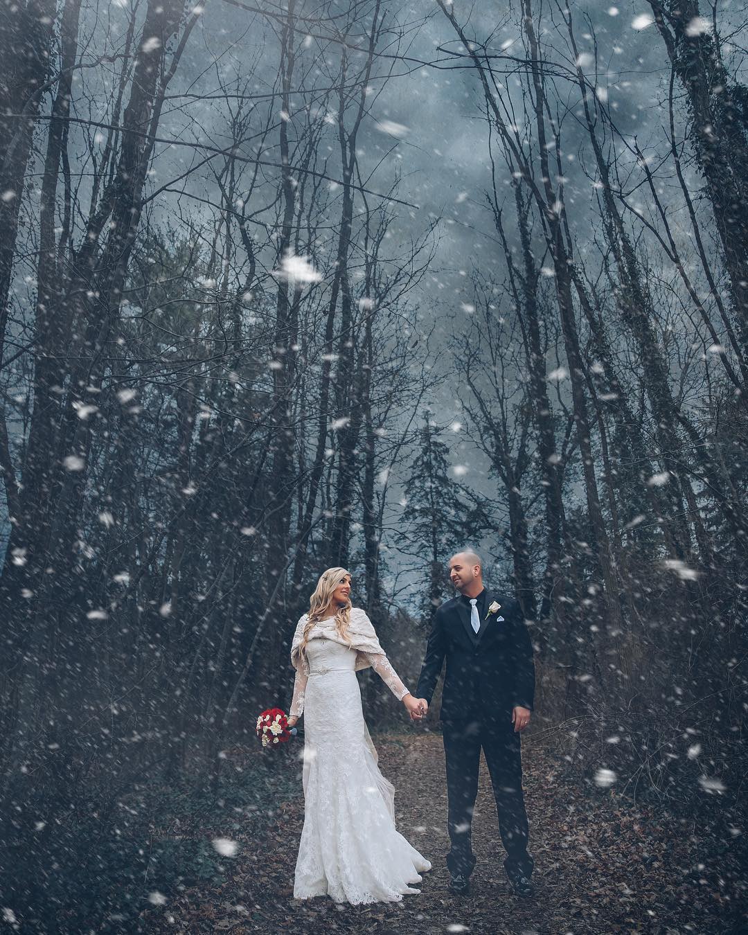 Bride and groom posing while holding hands as the snow falls