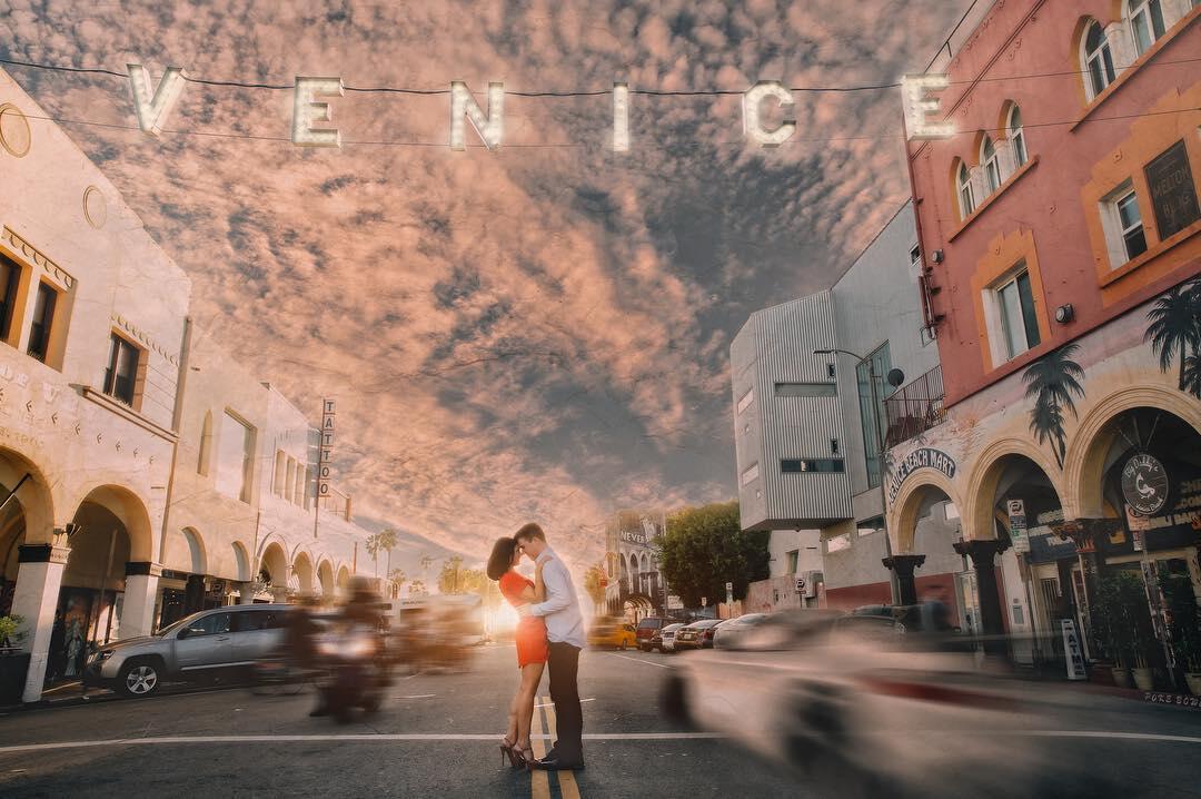 A couple posing for an engagement session in the middle of a road with LED Letter lights displaying - VENICE above them.