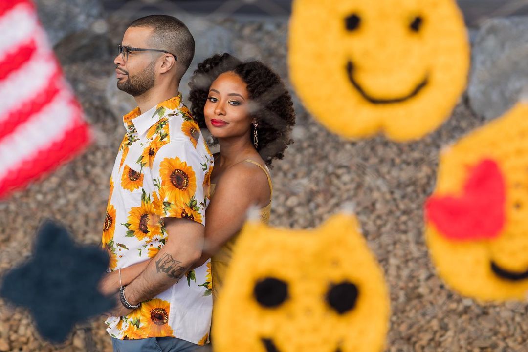 A couple photographed posing holding each other through a smiley painted glass 