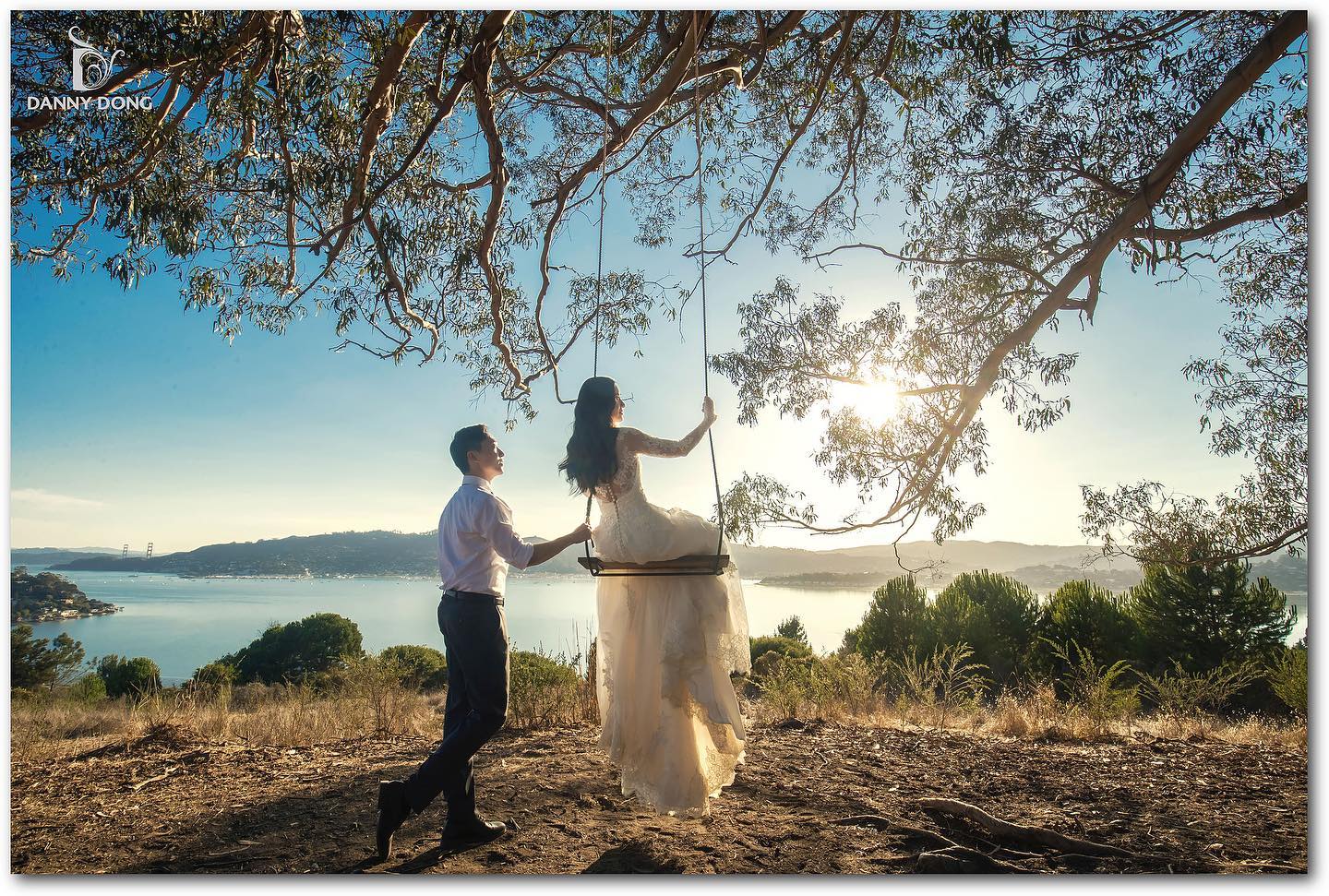 a bride is swinging on a swing under a tree while the groom stands beside her