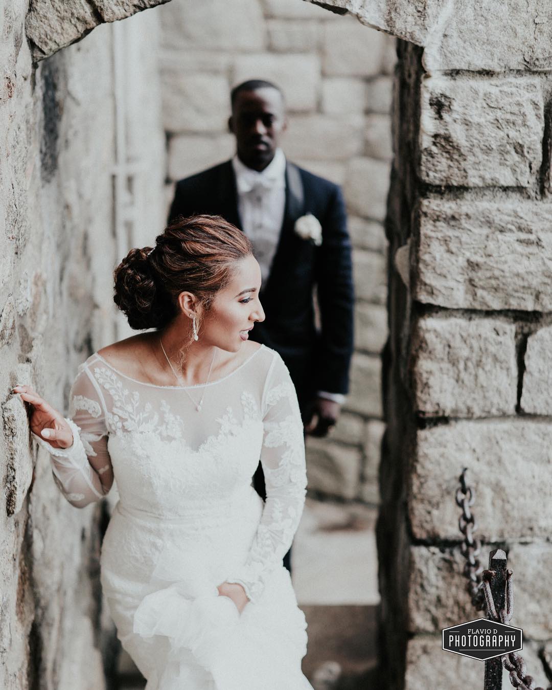 First look photo of a bride standing near a wall with groom standing behind her