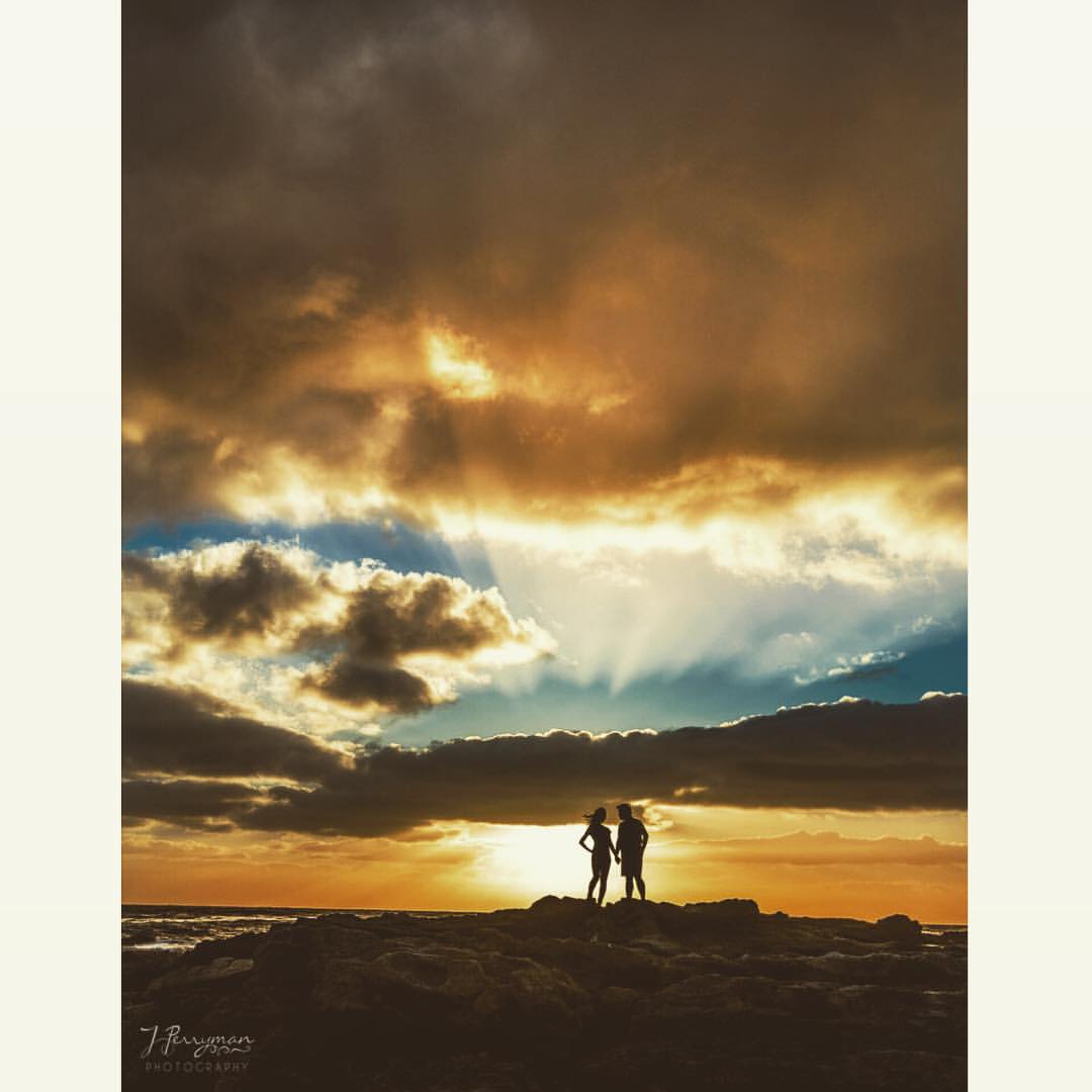 A silhouette of a couple posing near a beachside during sunset