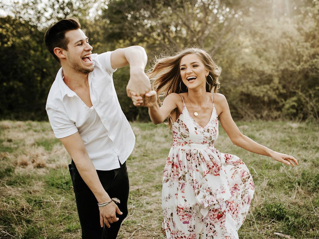 a groom twirling the bride in a grass field 