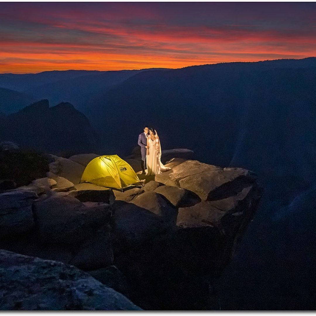 A couple posing near a camp while standing on top of a cliff during sunset