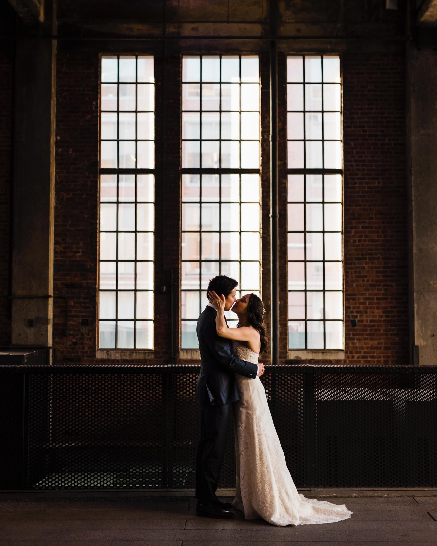 A couple holding each other and posing to kiss in front of a huge window