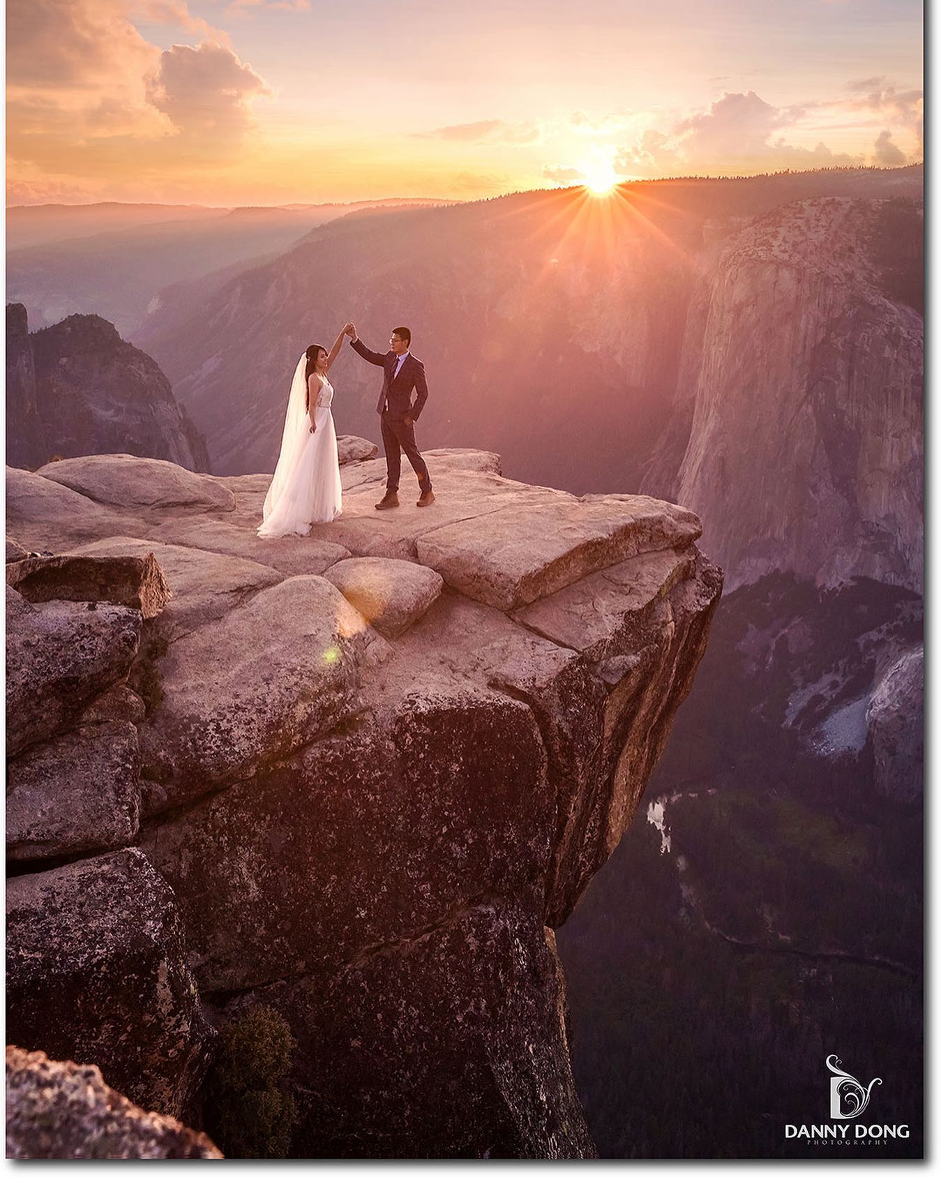 A bride and groom posing on top of a cliff as the sun sets behind the mountain peak