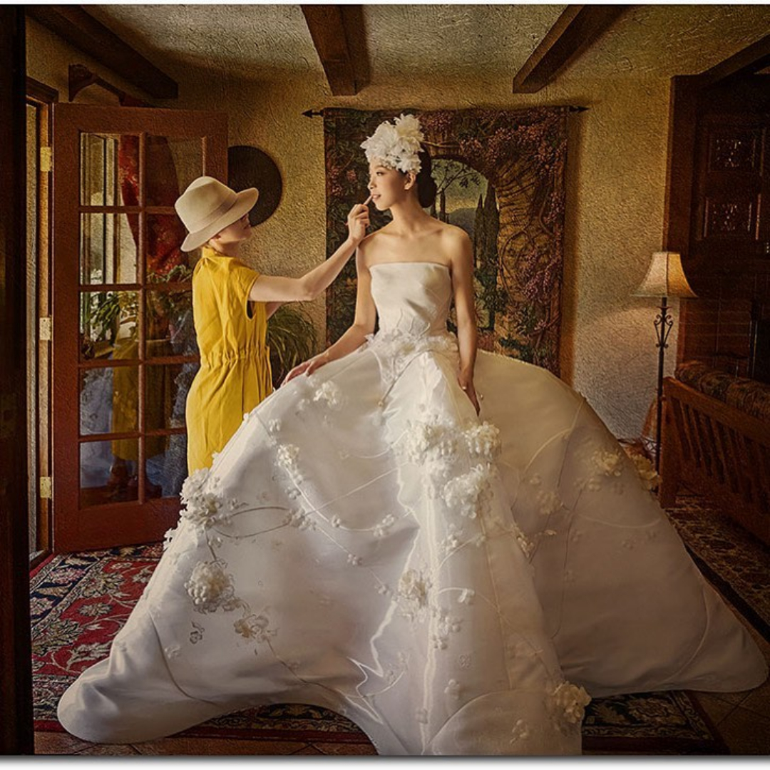 A bride stands in front of a doorway as the makeup artist fixes her makeup