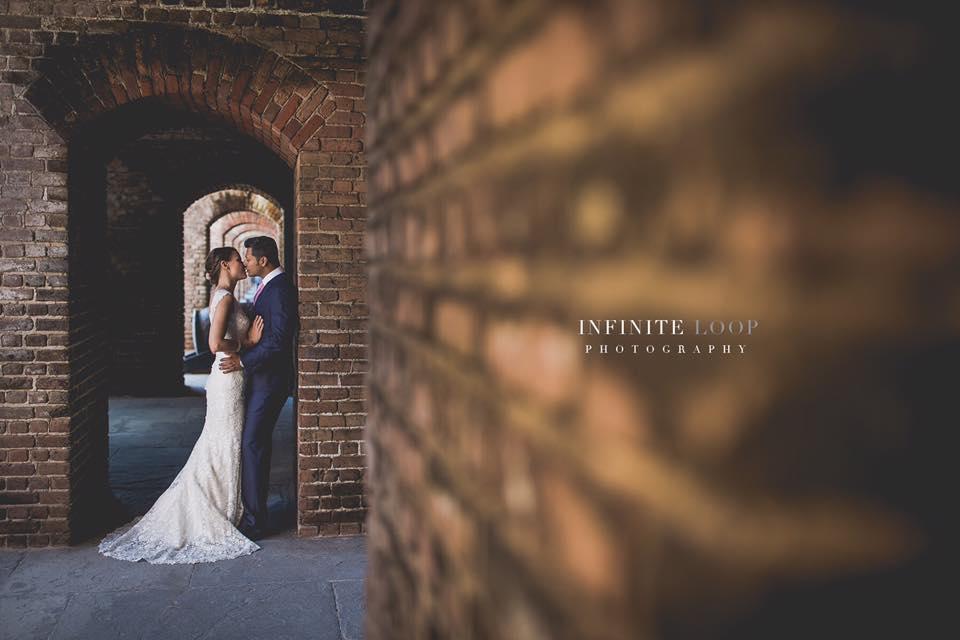 A bride and groom embracing against exposed brick.