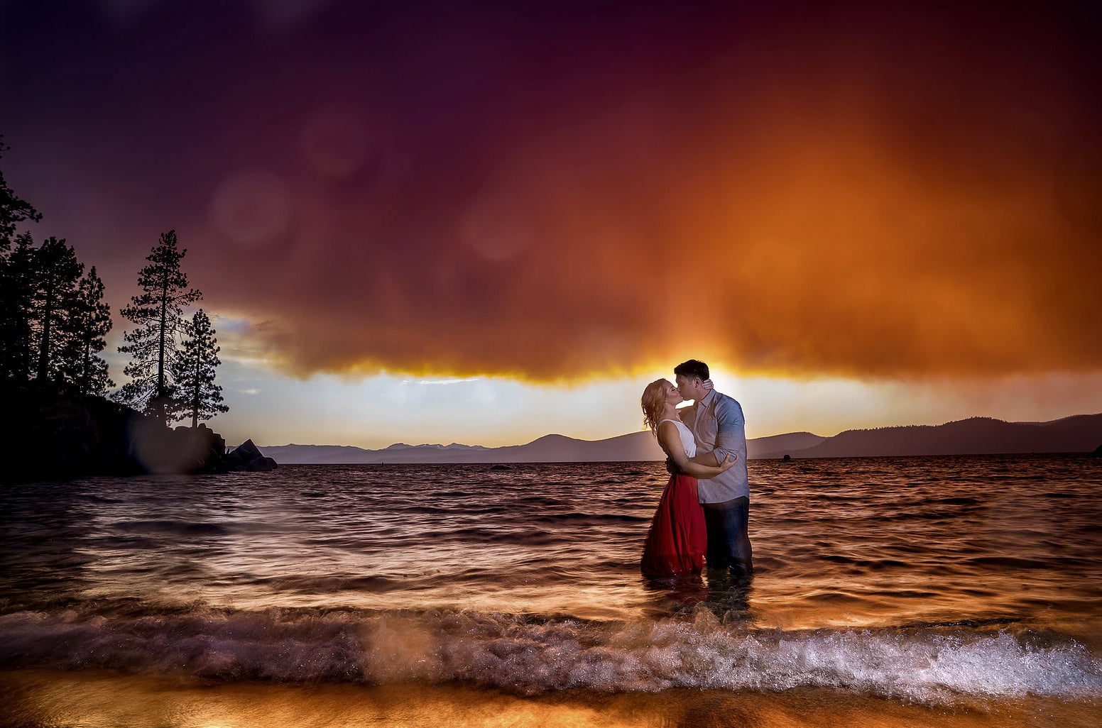 A couple kissing each other while standing on the beach with their feet immersed in seawater during sunset