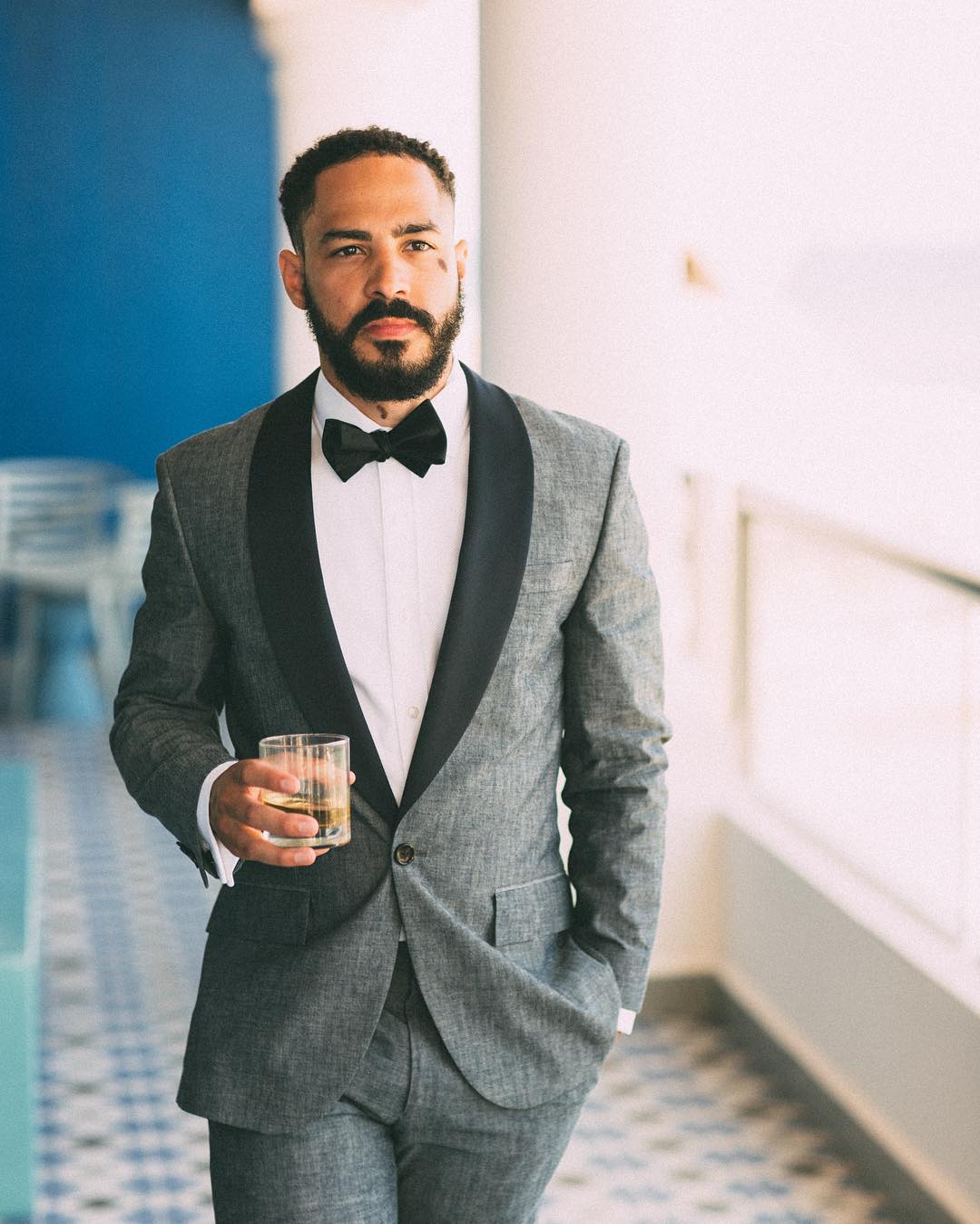 Portrait of a groom dressed in a tuxedo walking towards the camera while holding a glass