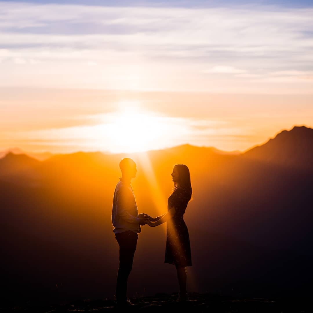 Silhouette of a couple looking at each other while holding hands as the Sun sets behind them
