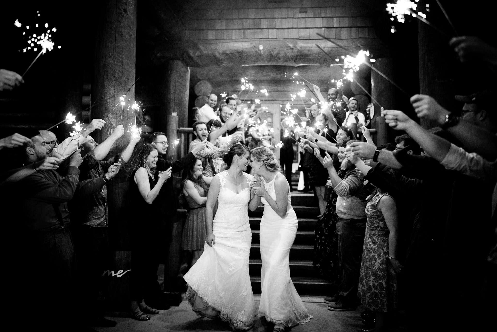 Black and white image of a couple of two brides walking through the exit as the guest lit sparklers 