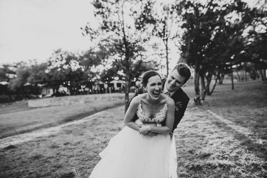 Black and white photo of a bride and groom laughing as they hug each other