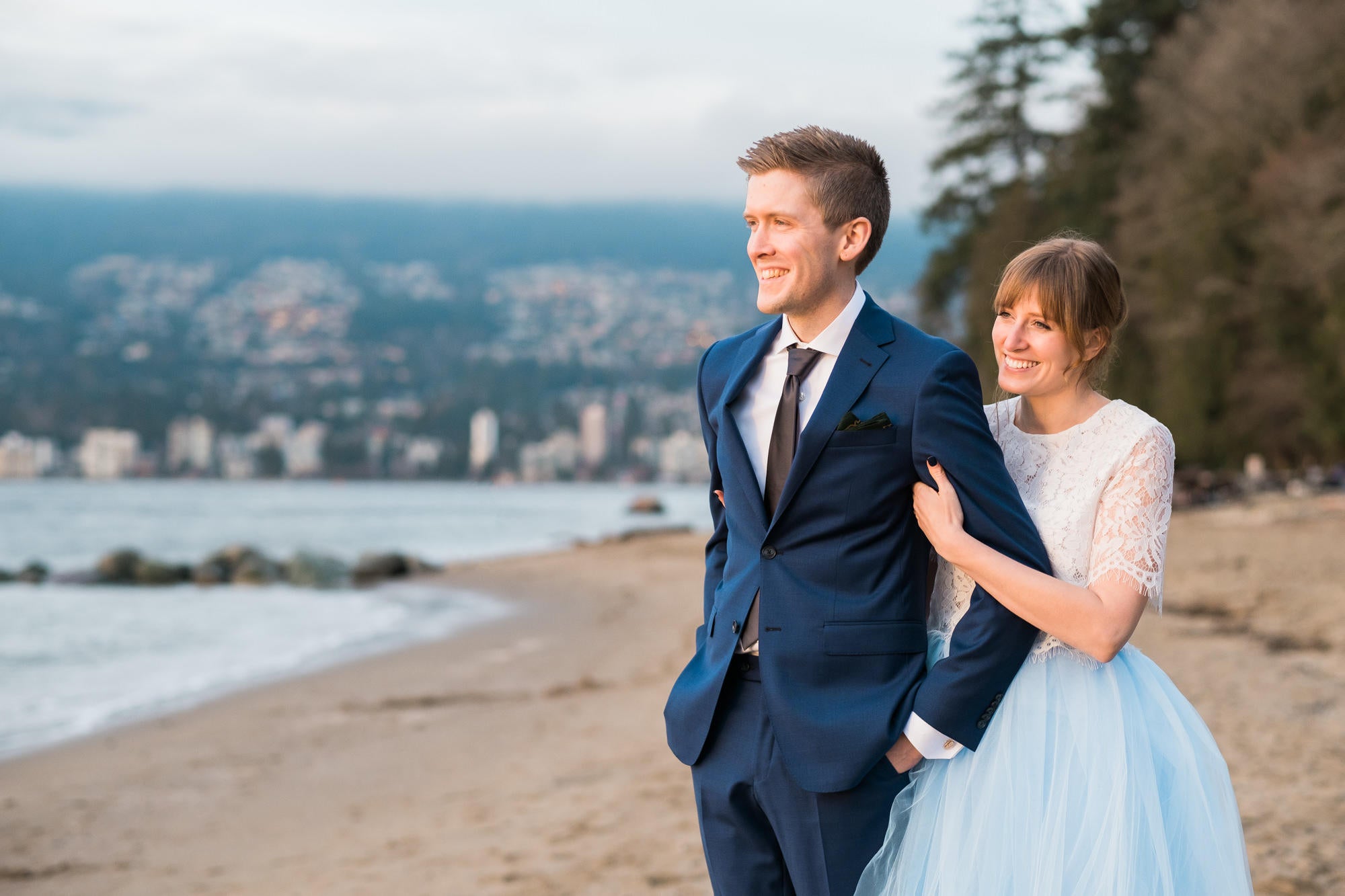 bride and groom walking arm in arm on a beach facing the sun