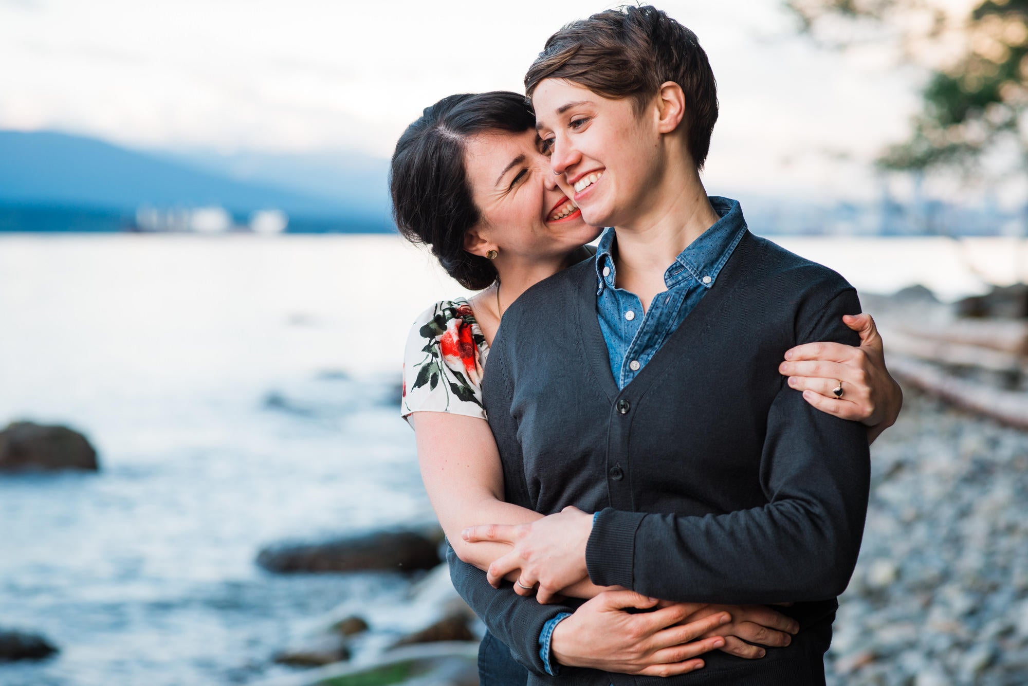 lesbian couple leaning into each other and sniggling on water's edge