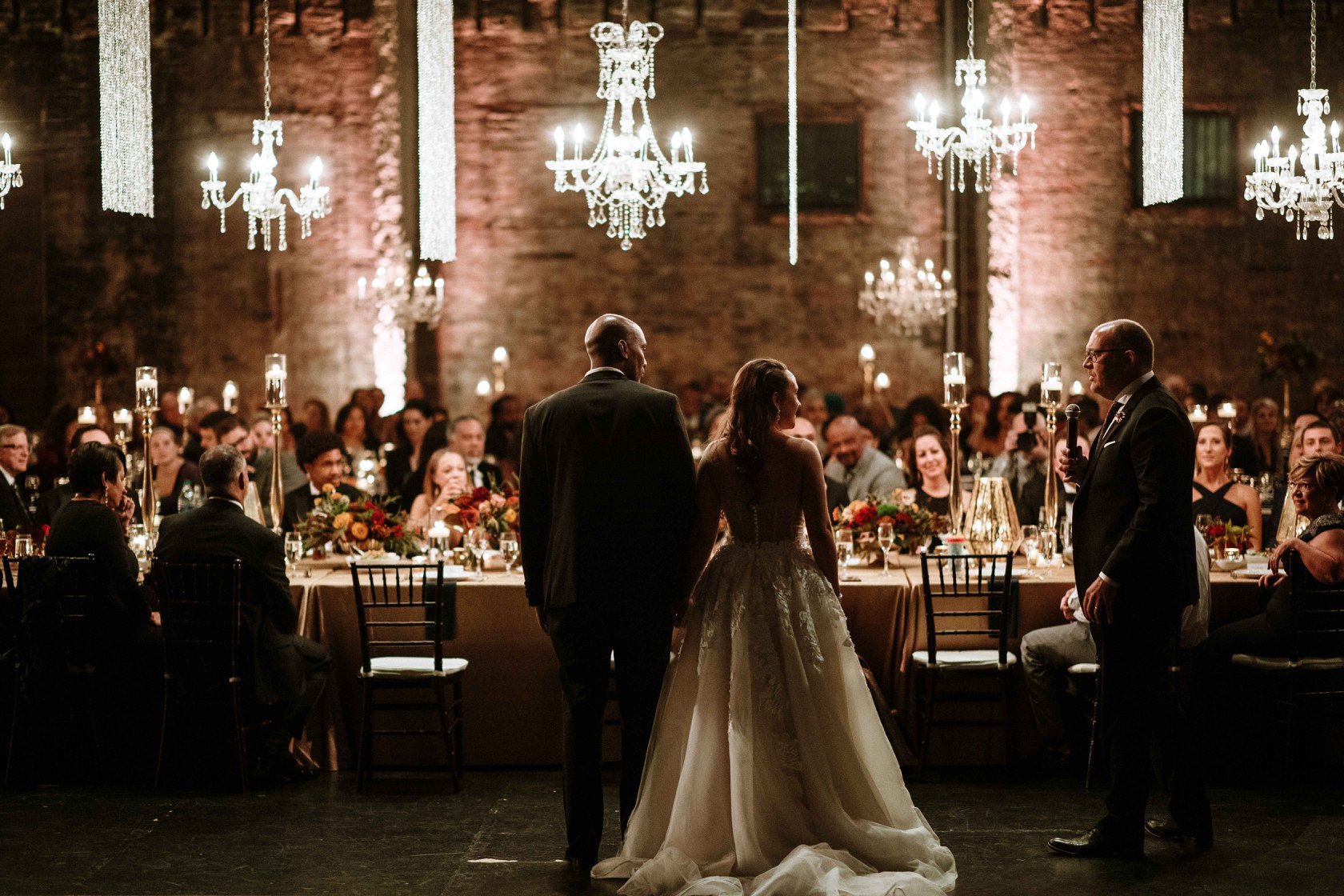 A person making a toast as the couple and guests watch over and listen