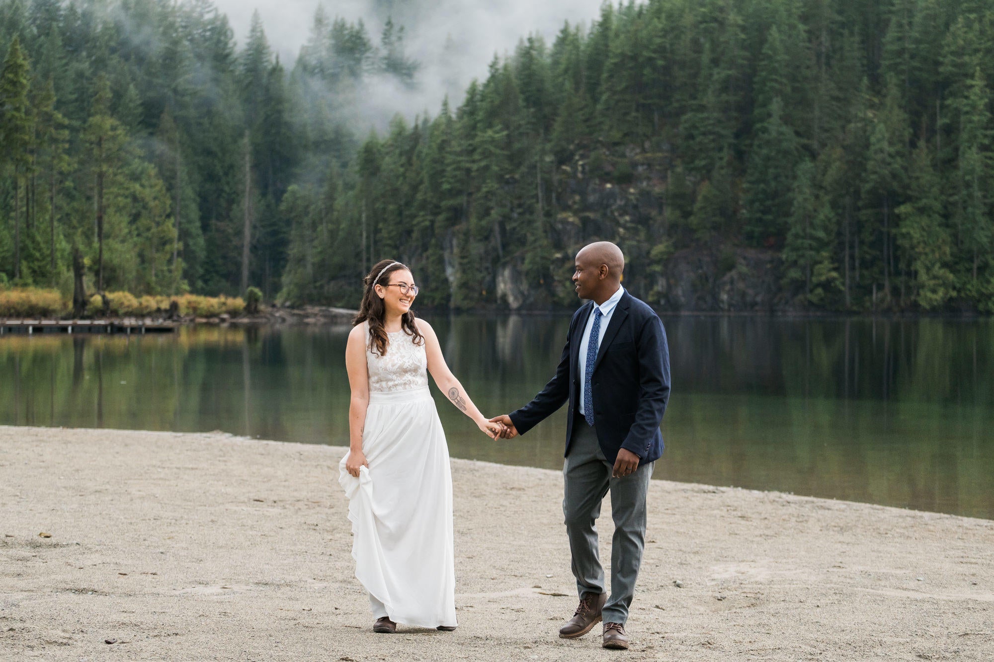 black groom holding the hand of a white bride on the edge of a lake with mist