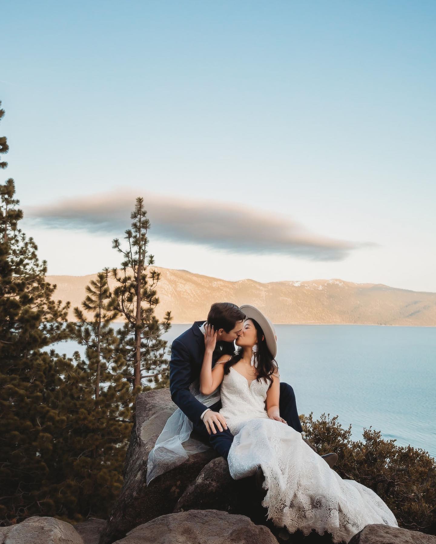 a couple kissing on a hilltop sitting on a rock