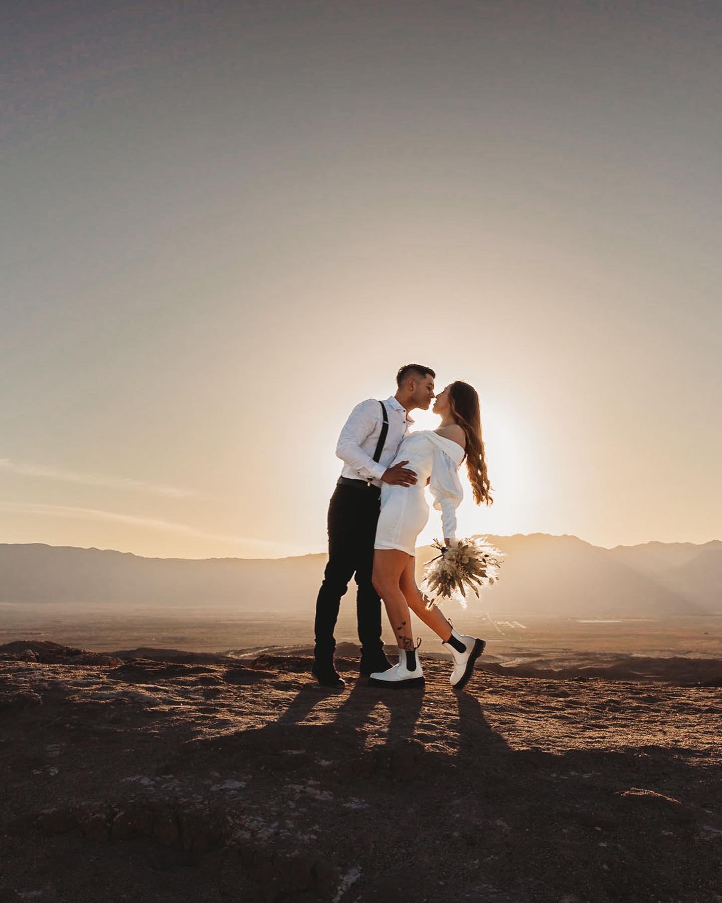 a wedding couple posing with the bouquet while the sun is shining from behind them