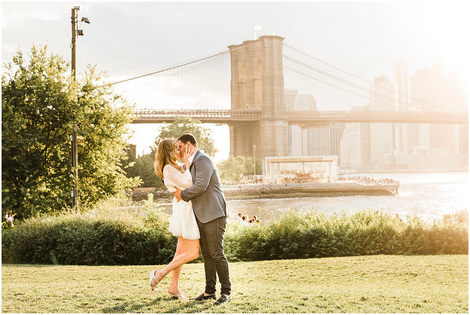 A couple kissing in front of a bridge by the lakeside