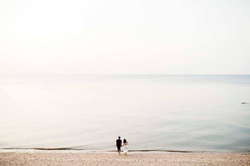 a wedding couple standing on a beach with the vast ocean in front of them