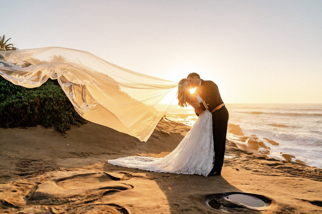 a wedding couple kissing while the bridal veil is blowing in the wind