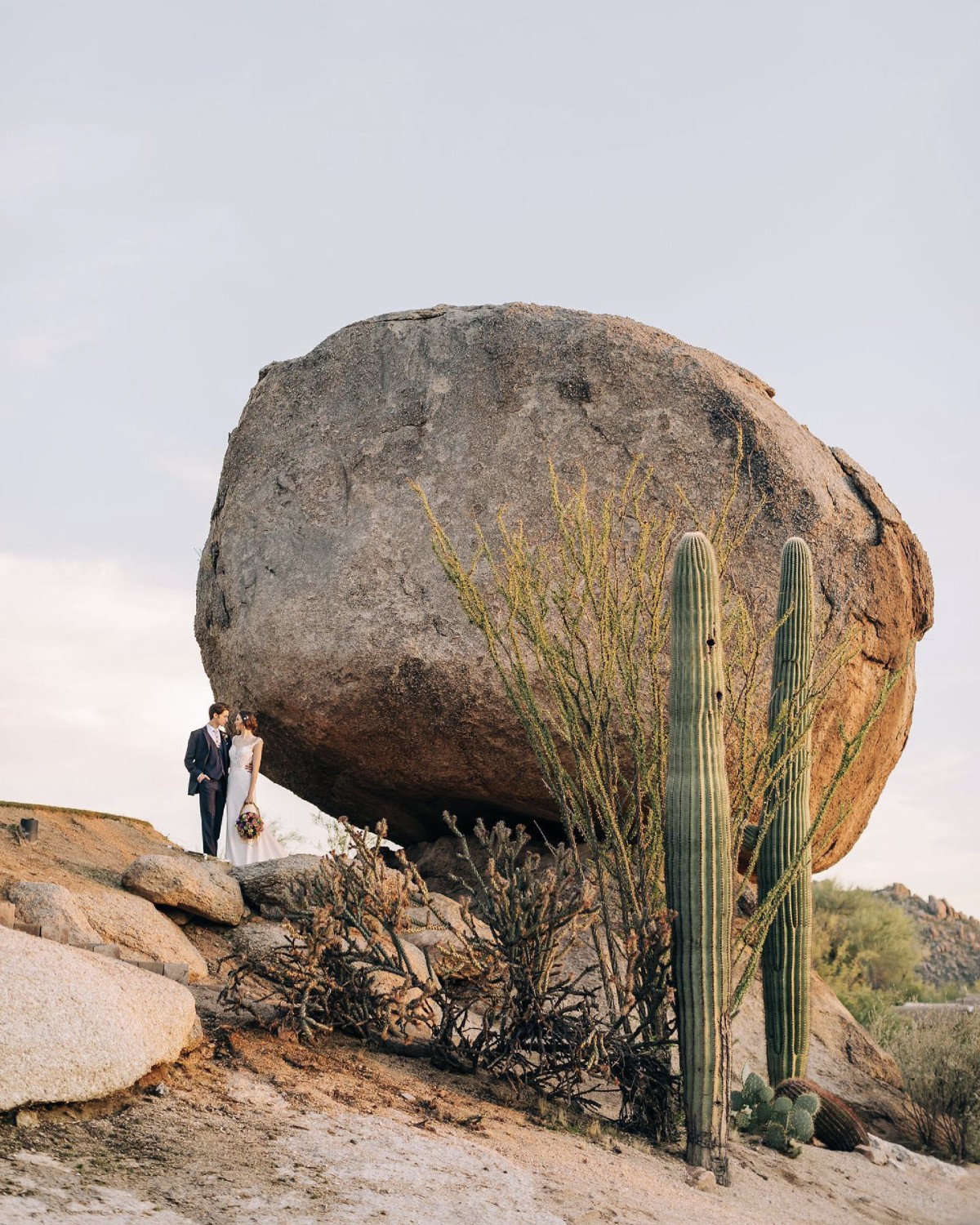 a wedding couple standing in front of a big boulder