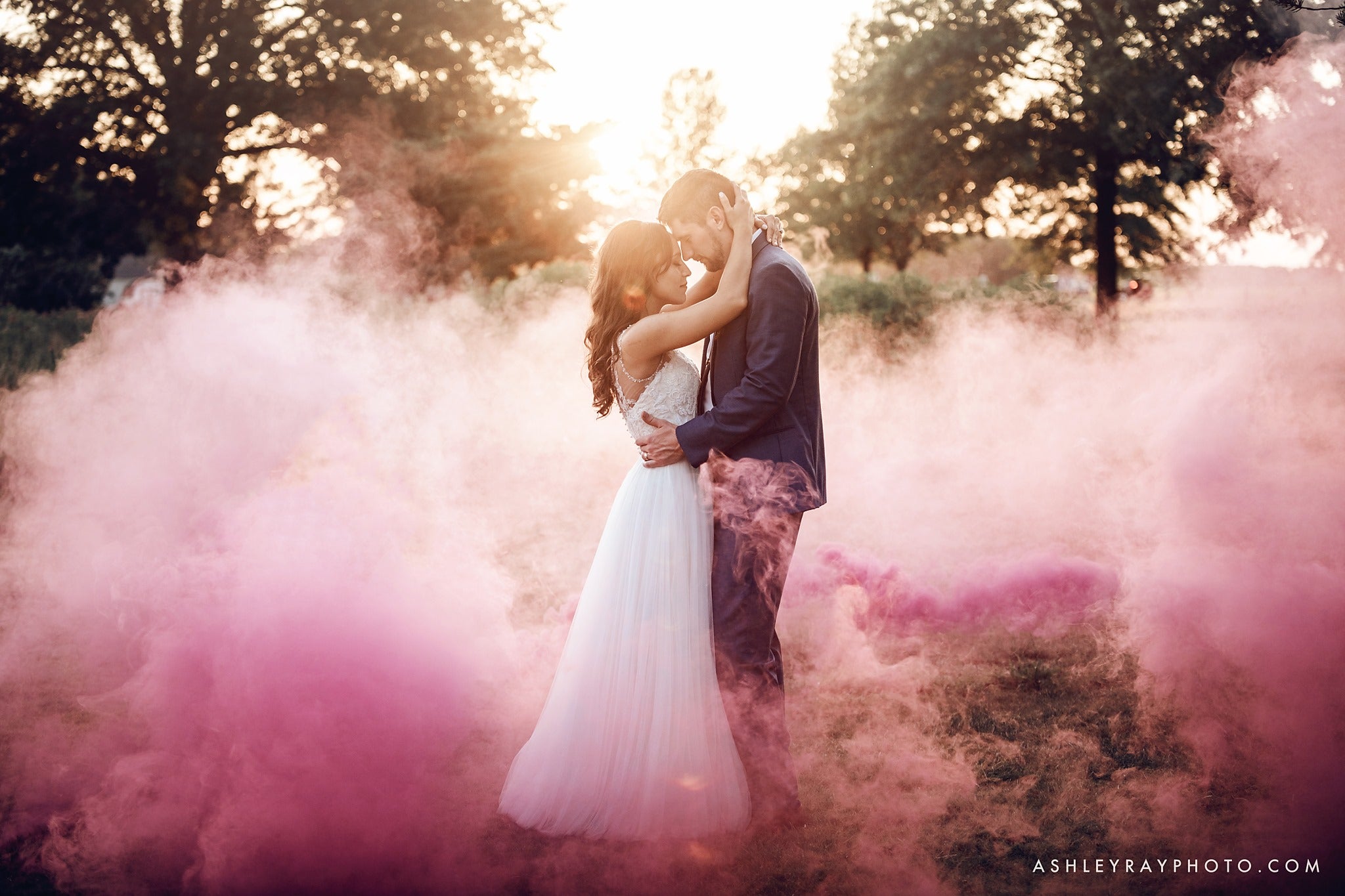 Bride and groom holding each other as a cloud of pink color smoke bomb surrounds them 