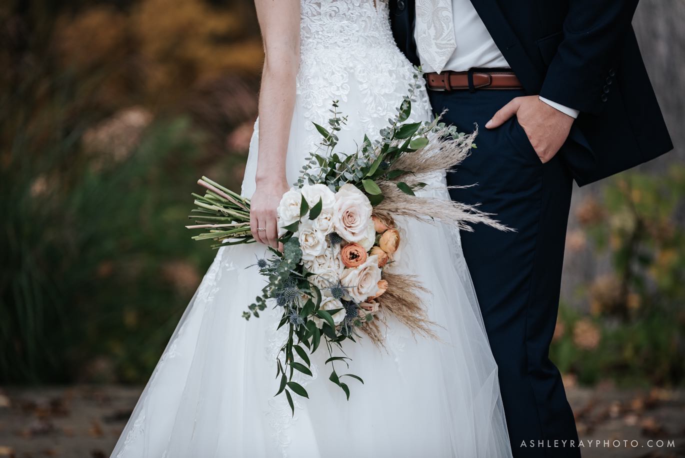 A close shot of a bride and groom posing together holding a bridal bouquet