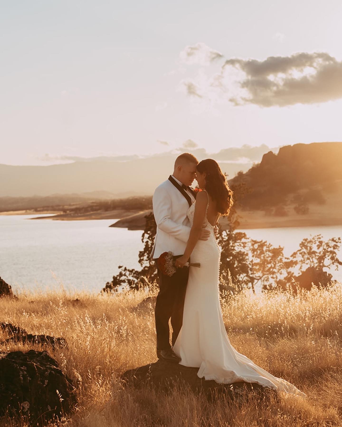 a wedding couple in their wedding attire sharing a close moment by cliffside