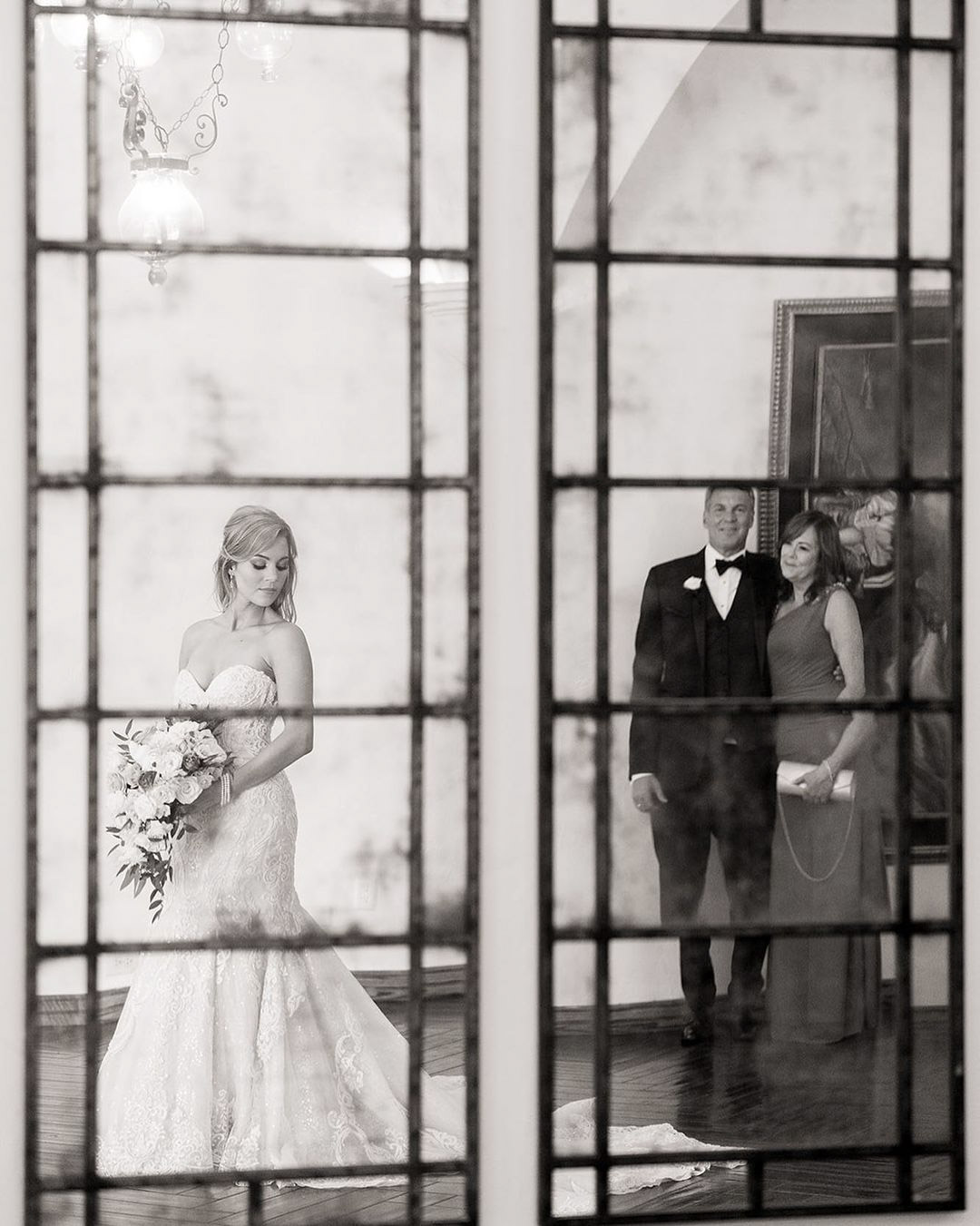 a bride to be in her bridal attire with the wedding bouquet while her parents stand behind