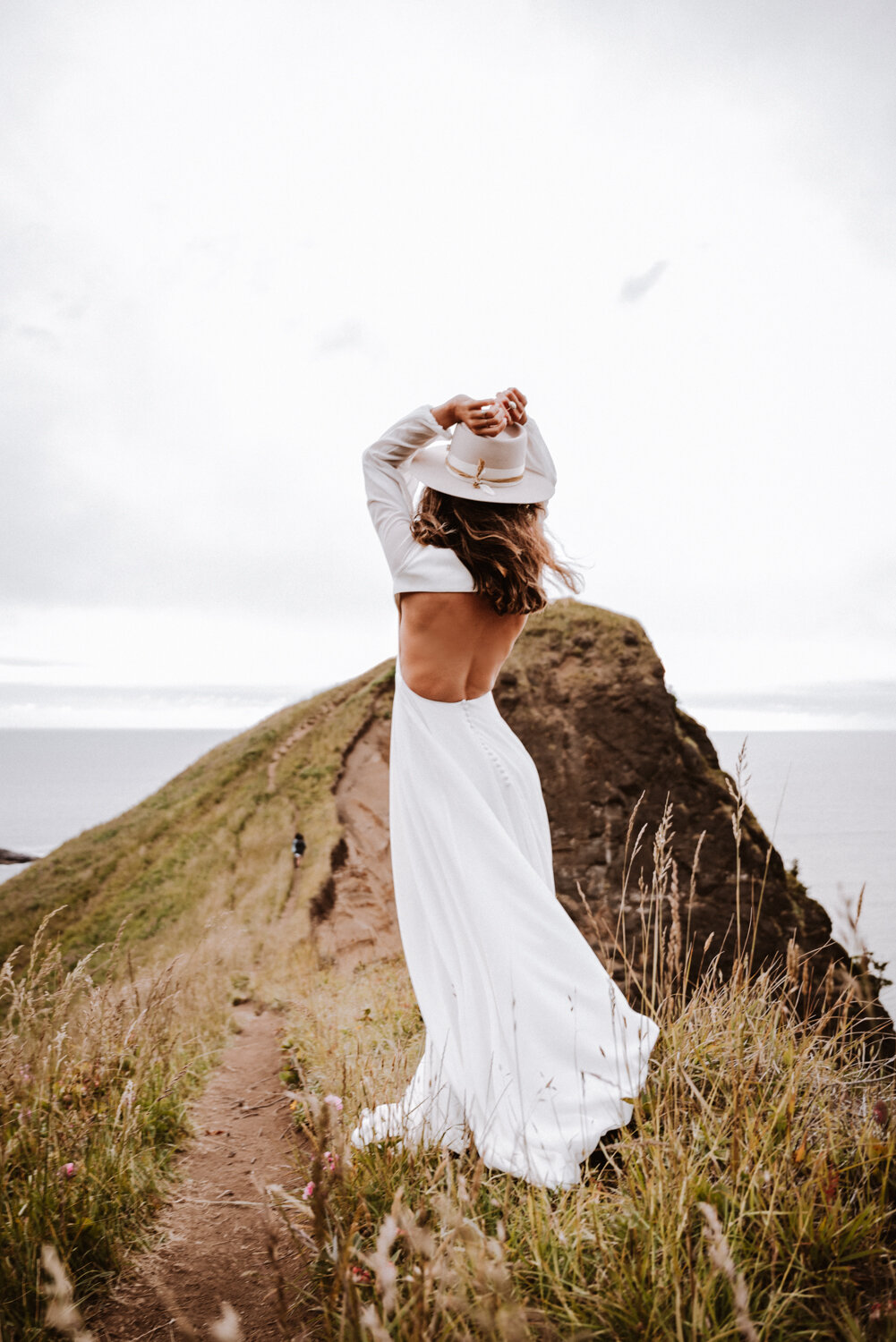 a bride in her wedding attire standing on top of a cliff by the waters