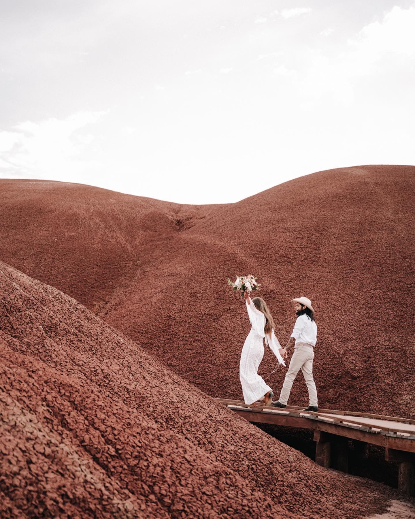 a wedding couple walking on a wooden bridge in their wedding attire