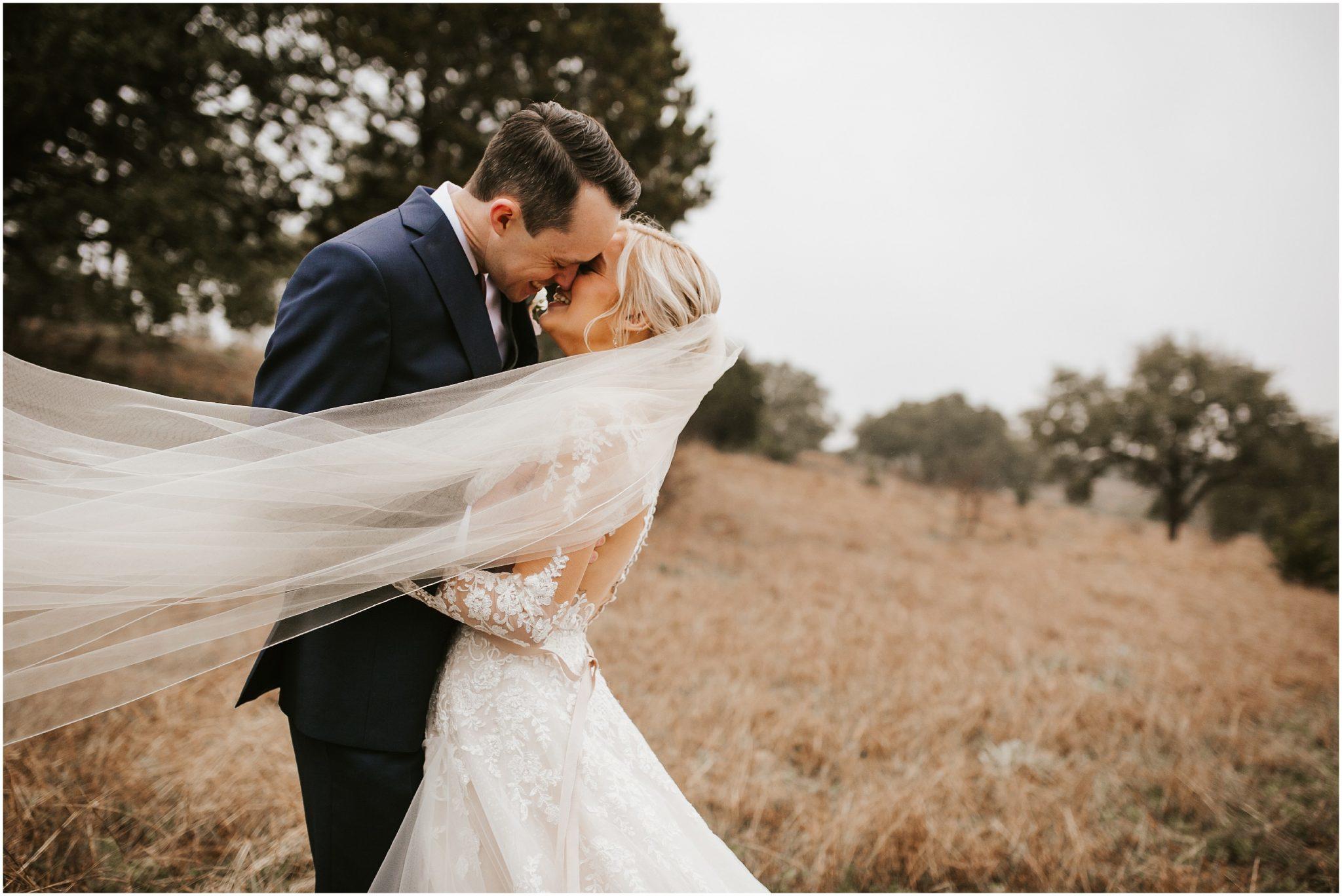 couple kissing and smiling in wedding attire in a brown grassy field