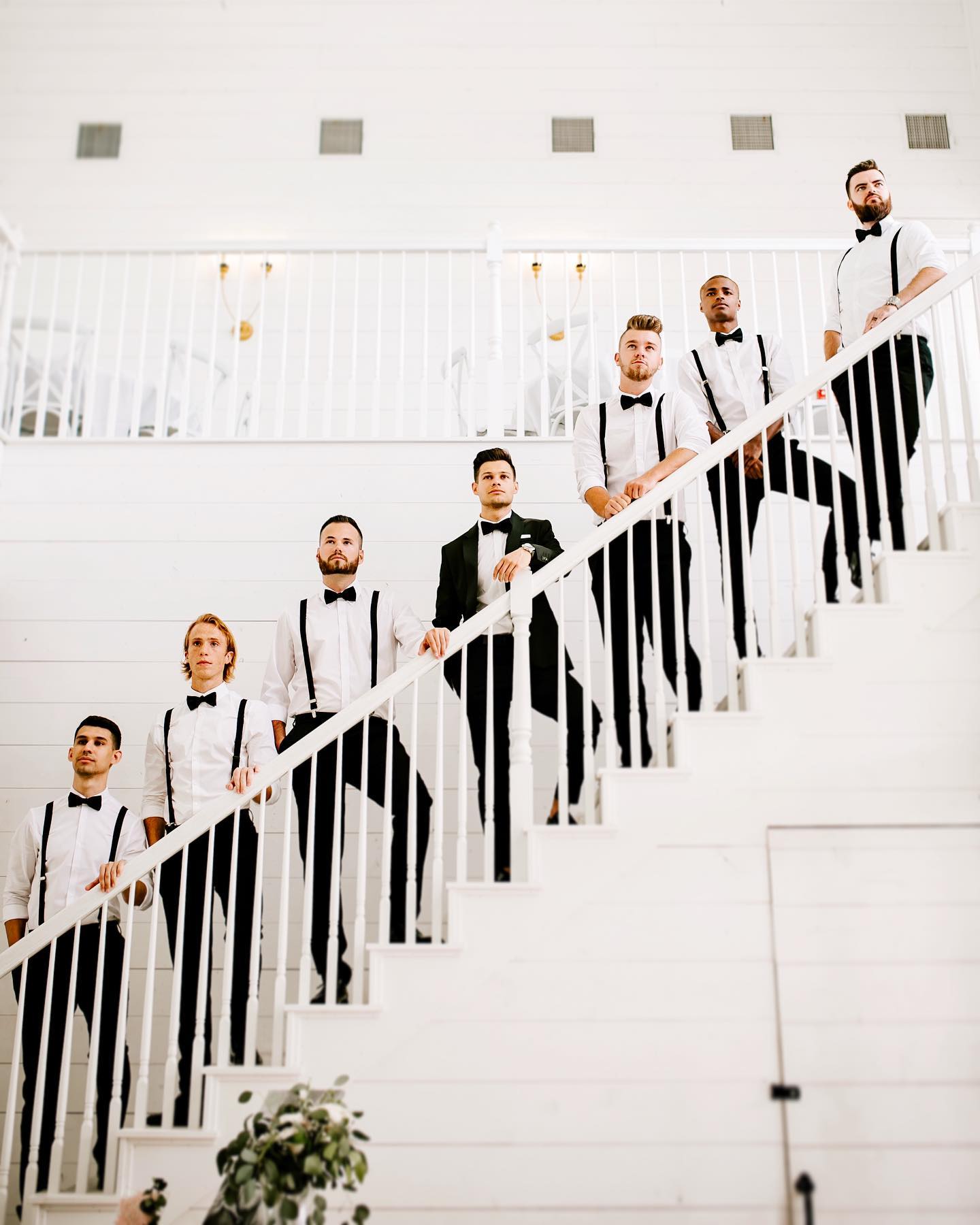 Groom and groomsmen pose while standing on a white-colored stairway 