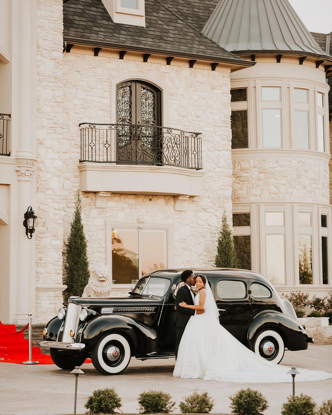 Bride and groom posing in front of a black car in front of a castle-themed building