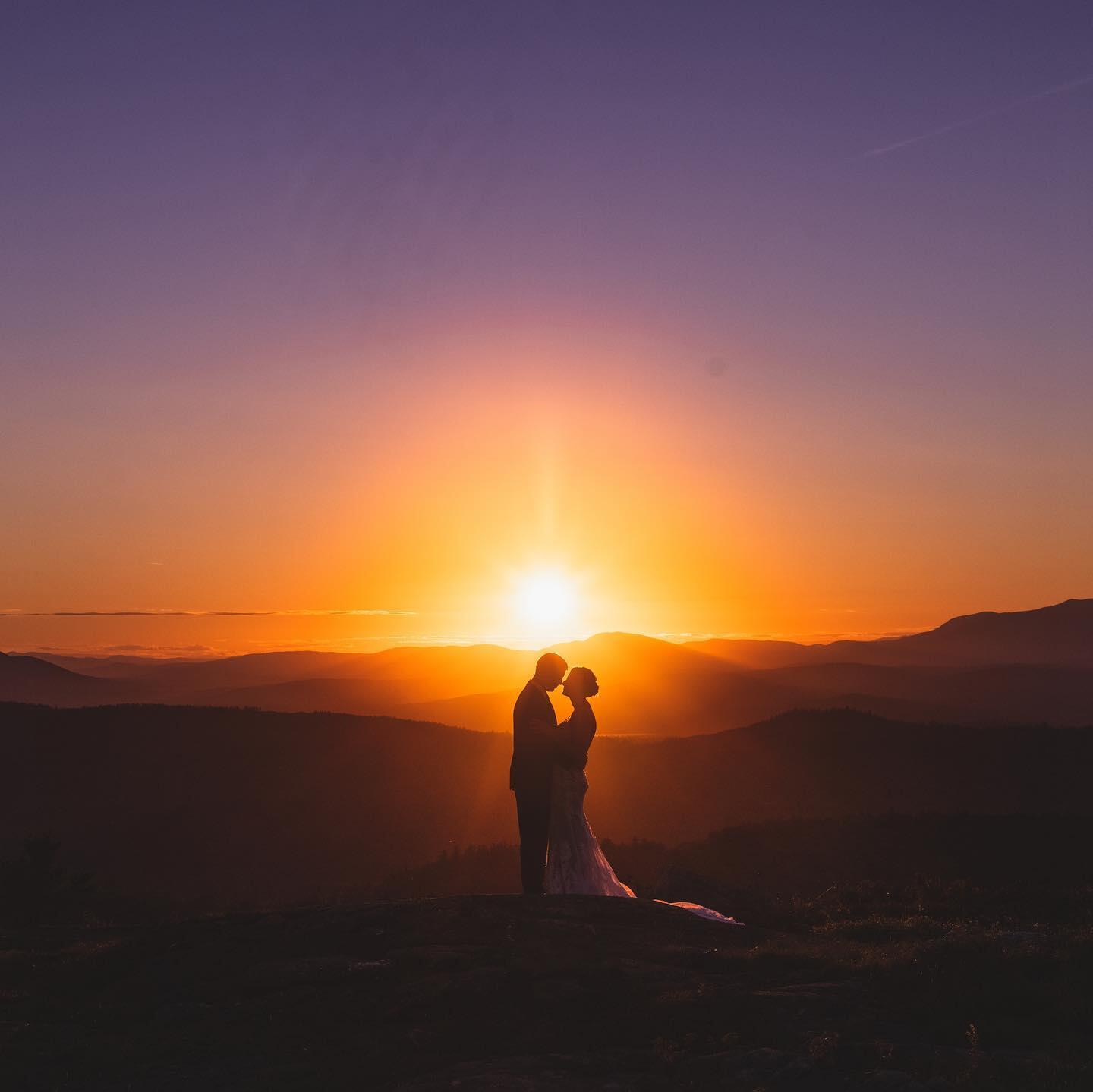 a silhouette of a couple holding each other during sunset with ranges of hills behind them