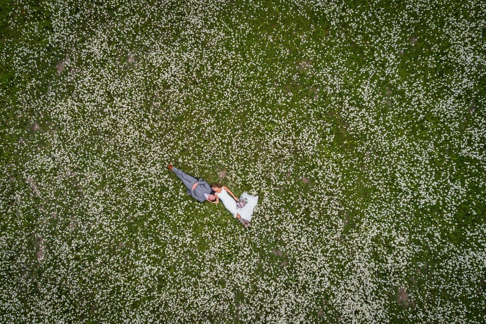 Aerial shot of a bride and groom lying on the field covered with white flowers