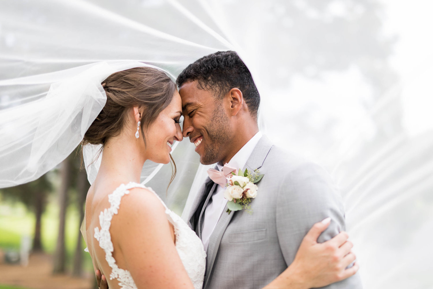 A portrait of a bride and groom leaning their foreheads towards each other and smiling