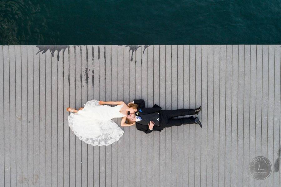 Drone shot of a bride and groom posing on a pavement near a sea