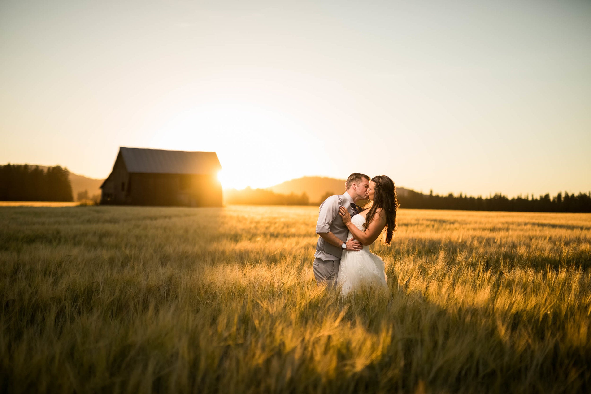 A portrait of a bride and groom kissing during sunset at a field