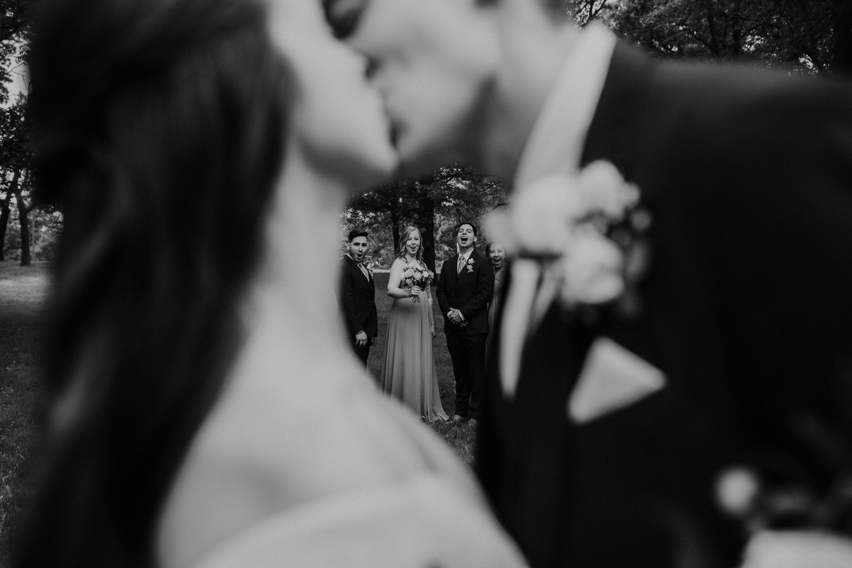 a creative monochrome close up shot of a couple kissing and their friends visible between them