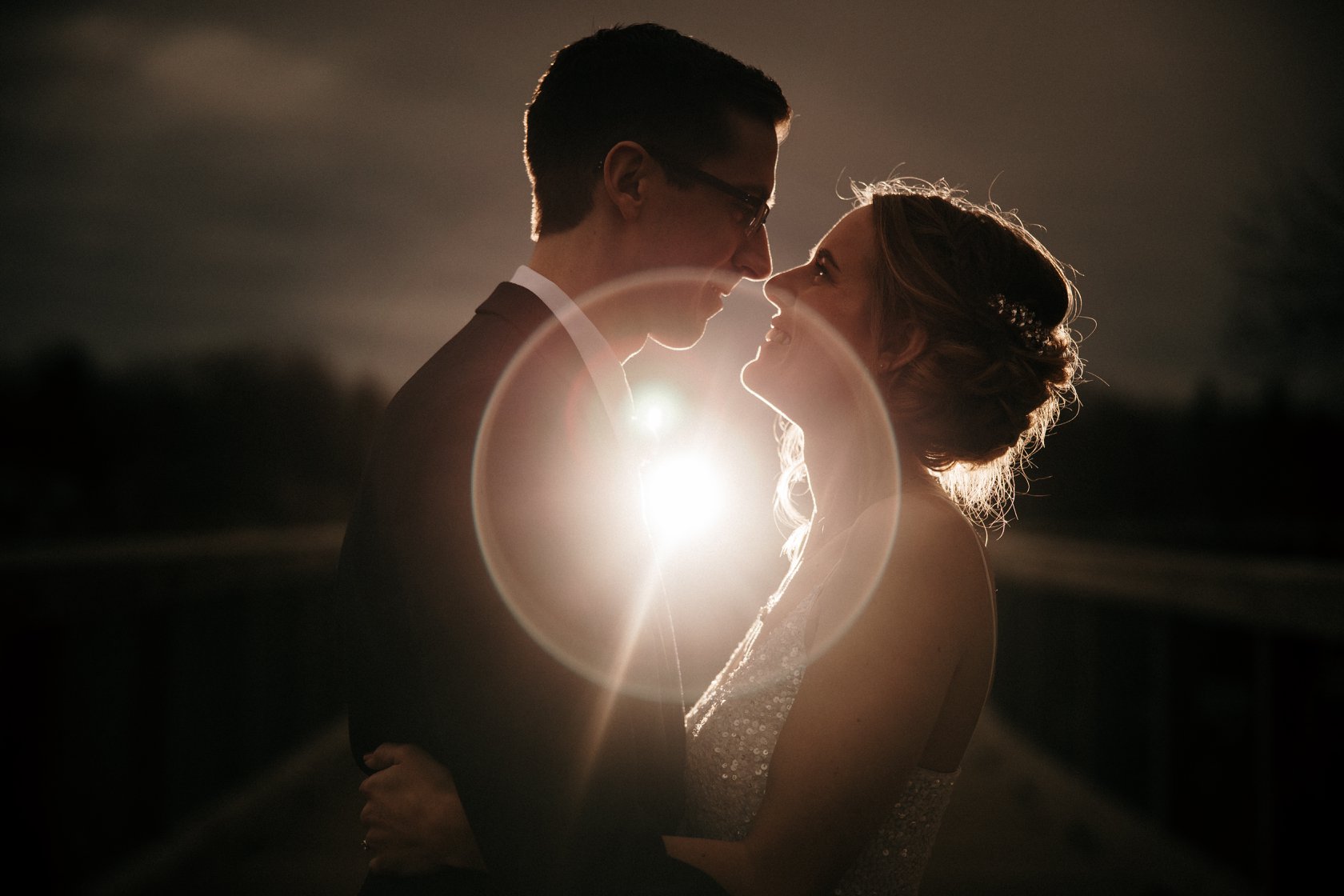 Portrait of a bride and groom looking at each other as the lens flare creates a halo effect in between them 